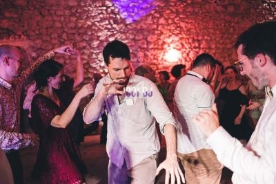 Des personnes dansent dans une ambiance festive avec un éclairage tamisé et des murs en pierre en arrière-plan.