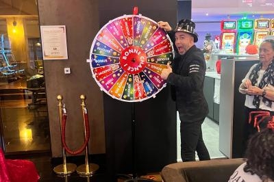 Un homme tourne une roue de la chance colorée dans un espace intérieur avec des machines à sous en arrière-plan.