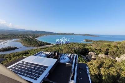 Vue d'un poste de DJ avec ordinateur et platines, surplombant une baie entourée de végétation et de collines.