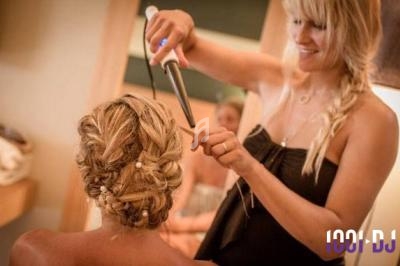 Une coiffeuse réalise une coiffure tressée avec des perles sur une femme, utilisant un fer à boucler.