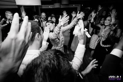 Groupe de personnes dansant et levant les mains lors d'une fête dans une ambiance festive en noir et blanc.