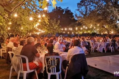Groupe de personnes assises à des tables en extérieur, sous des guirlandes lumineuses, lors d'un événement en soirée.