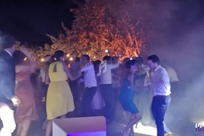 Personnes dansant en soirée en plein air, éclairées par des lumières colorées et entourées de fumée.