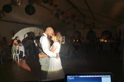 Un couple danse sous un éclairage tamisé dans une salle décorée, entouré d'invités assis à des tables.