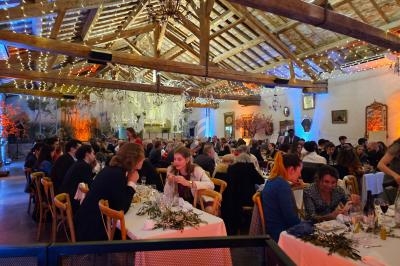 Salle de réception décorée avec des guirlandes lumineuses, remplie d'invités assis à des tables pour un dîner.