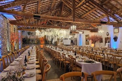 Salle de réception rustique avec tables dressées, décorations florales suspendues et éclairage chaleureux.