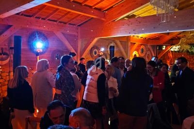 Groupe de personnes discutant dans une salle en bois éclairée par des lumières chaudes, avec un lustre visible au plafond.