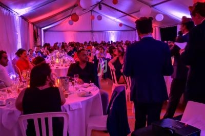 Des invités assis à des tables rondes dans une tente décorée, éclairée par des lumières tamisées et des lanternes suspendues.