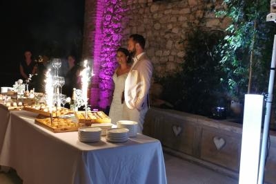 Un couple en tenue de mariage se tient près d'une table de desserts illuminée par des fontaines de lumière.