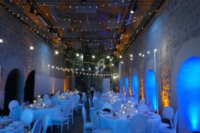 Salle voûtée décorée pour un événement, avec tables rondes dressées, éclairage tamisé et guirlandes lumineuses.