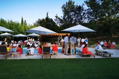 Groupe de personnes réunies en extérieur sur une terrasse avec parasols, transats et pelouse environnante.