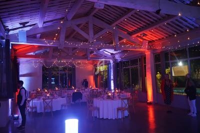 Salle de réception décorée avec des guirlandes lumineuses, tables dressées et éclairage tamisé coloré.