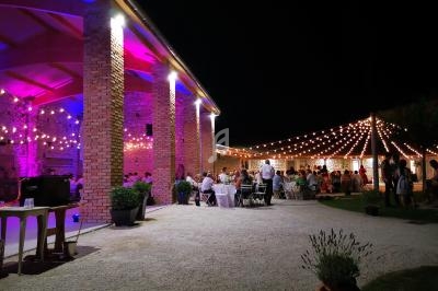 Cour extérieure éclairée de guirlandes lumineuses, avec des invités assis à des tables lors d'un événement nocturne.