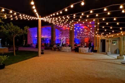 Guirlandes lumineuses suspendues éclairant une réception nocturne en extérieur avec tables dressées et murs en pierre.