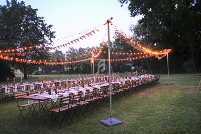 Tables longues décorées et éclairées par des guirlandes lumineuses dans un jardin en soirée.