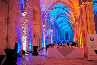 Salle voûtée éclairée de lumières colorées avec tables de réception et un panneau publicitaire visible à droite.