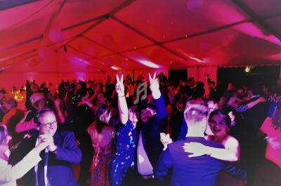 Des personnes dansent sous une grande tente éclairée de lumières roses lors d'une fête ou d'un événement festif.