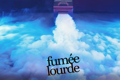 Machine diffusant une épaisse fumée blanche au sol dans une ambiance lumineuse bleutée.