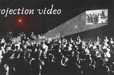 Une foule assiste à une projection vidéo en noir et blanc, avec un projecteur illuminant un écran.