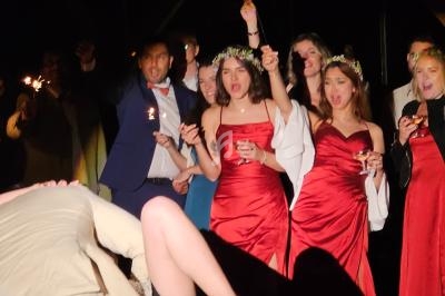 Des invités en tenue de soirée, dont des femmes en robes rouges, célèbrent avec des étincelles dans un cadre festif.
