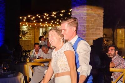 Un couple danse joyeusement sous des guirlandes lumineuses dans un cadre extérieur en soirée.