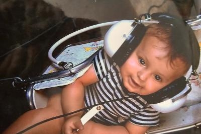 Bébé souriant assis dans une chaise haute, portant un casque audio surdimensionné.