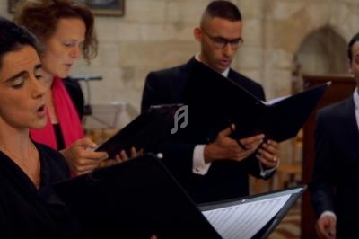 Quatre chanteurs en tenue formelle interprètent une œuvre vocale dans un lieu au style architectural ancien.