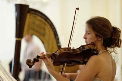 Une femme joue du violon devant une harpe dans une salle lumineuse.