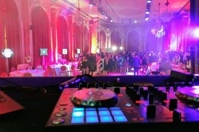 Vue d'une salle de réception élégante avec des invités debout, éclairages colorés et une table de mixage au premier plan.