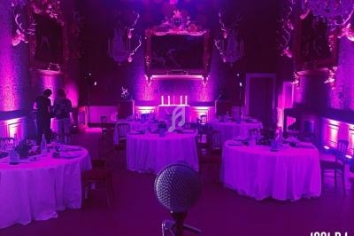 Salle de réception éclairée en rose avec tables rondes dressées, vue depuis un micro au premier plan.