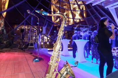 Un saxophone posé sur une scène en bois lors d'un événement dans un espace vitré avec des invités en arrière-plan.