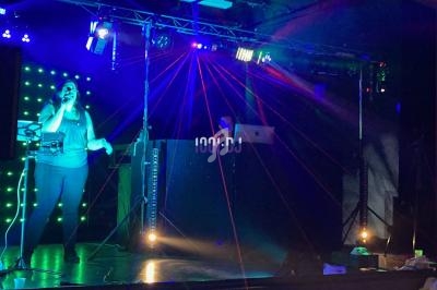 Une chanteuse sur scène avec un DJ en arrière-plan, éclairés par des lumières colorées et des lasers rouges.