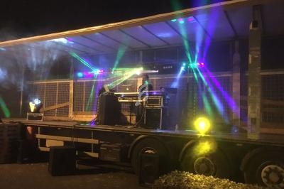 Un DJ mixe sur une scène extérieure éclairée par des jeux de lumière colorés, de nuit.