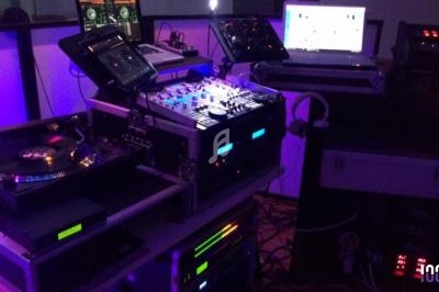 Équipement de DJ comprenant platine vinyle, table de mixage, ordinateurs et éclairage coloré en arrière-plan.