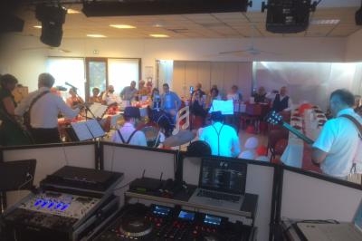 Un groupe de musiciens joue devant un public assis dans une salle éclairée, vue depuis une console de mixage.
