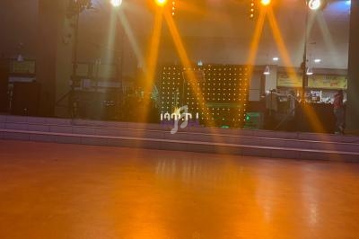 Scène éclairée par des projecteurs orange avec des équipements audio et un fond lumineux à LED.