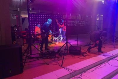 Groupe de musiciens jouant sur une scène éclairée par des lumières colorées dans une ambiance intérieure.