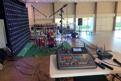 Console de mixage audio et micros devant une scène équipée de batteries, micros et éclairage LED.