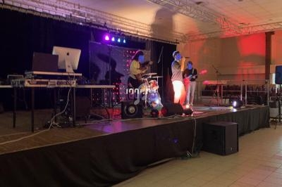 Un groupe de musique joue sur une scène éclairée, avec des instruments et des équipements audio visibles.