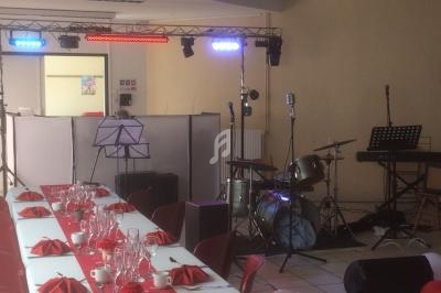 Salle décorée pour un événement avec tables dressées et une scène équipée d'instruments de musique et éclairages.