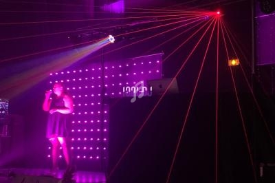 Une chanteuse sur scène éclairée par des lumières violettes et des lasers rouges, avec un fond lumineux.