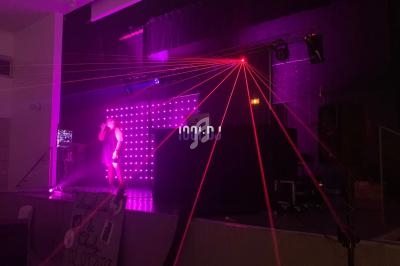 Un chanteur sur scène avec des lumières laser rouges et un écran lumineux en arrière-plan.