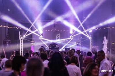 Foule dansante sous des jeux de lumière colorés avec un DJ sur scène dans une ambiance festive.