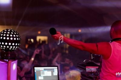 Un DJ anime une soirée en boîte de nuit, tenant un micro face à une foule dansante sous des lumières colorées.