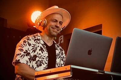 Un homme souriant, portant un chapeau et un casque audio, mixe de la musique sur un ordinateur portable.