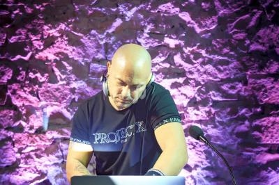 Un DJ mixe de la musique sur un ordinateur portable devant un mur en pierre éclairé par des lumières colorées.