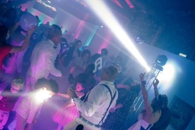 Des personnes dansent sous des lumières colorées dans une ambiance festive, avec un DJ en arrière-plan.