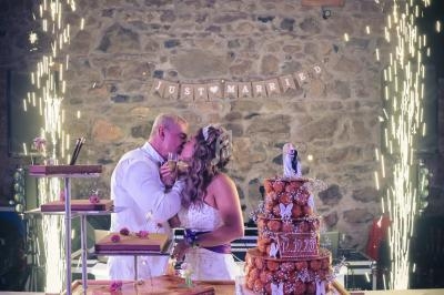 Un couple de mariés s'embrasse devant une table décorée avec des desserts et un gâteau, sous des étincelles festives.