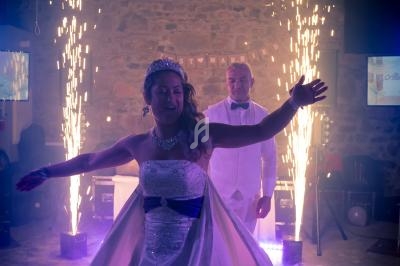 Un couple en tenue de mariage danse au milieu de fumée et d'étincelles dans une salle en pierre.