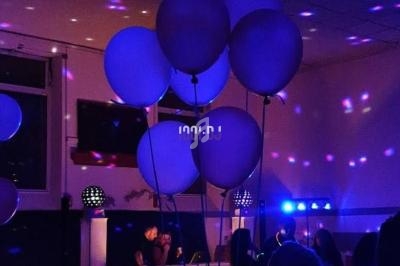 Des ballons flottent dans une salle sombre éclairée par des lumières colorées, avec un DJ en arrière-plan.